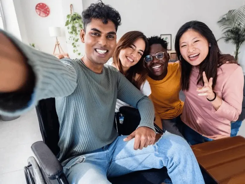 Four diverse friends, one disabled in wheelchair, all laughing an smiling taking photo together