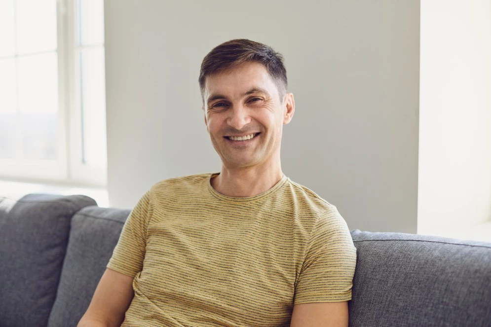 Happy man sitting on couch at home smiling at camera