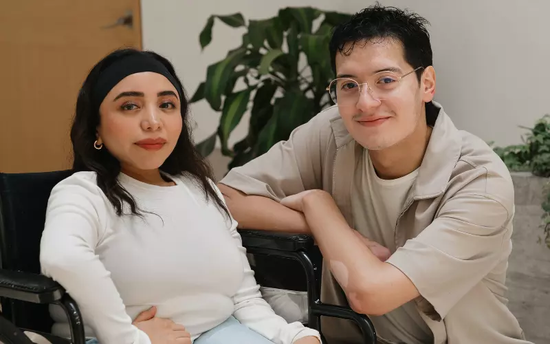 Woman in a wheelchair smiling at the camera alongside a support worker