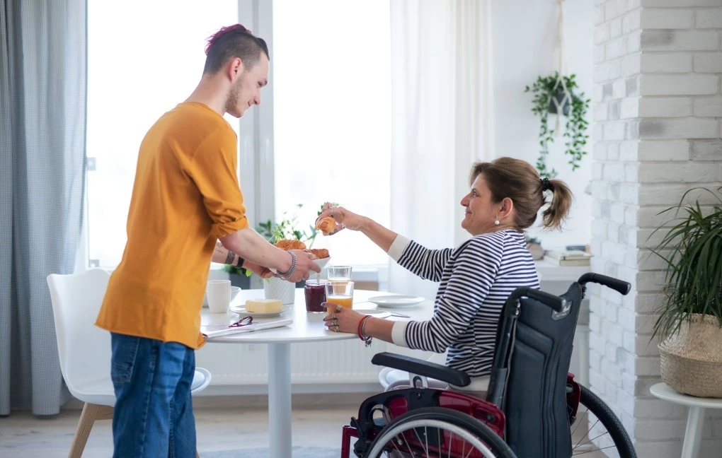 Woman in a wheelchair taking a croissant from a plate with a support worker nearby