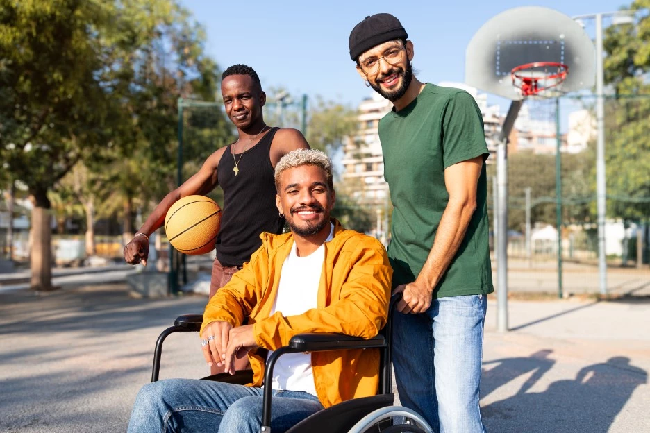 Three friends, one man disabled in wheelchair, outside on basketball court smiling at camera