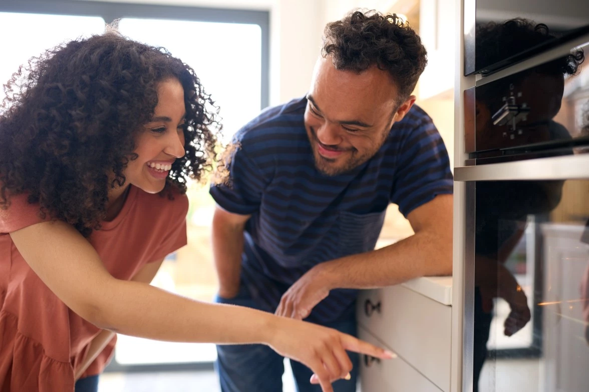 Man with Down syndrome and a carer checking food cooking in an oven