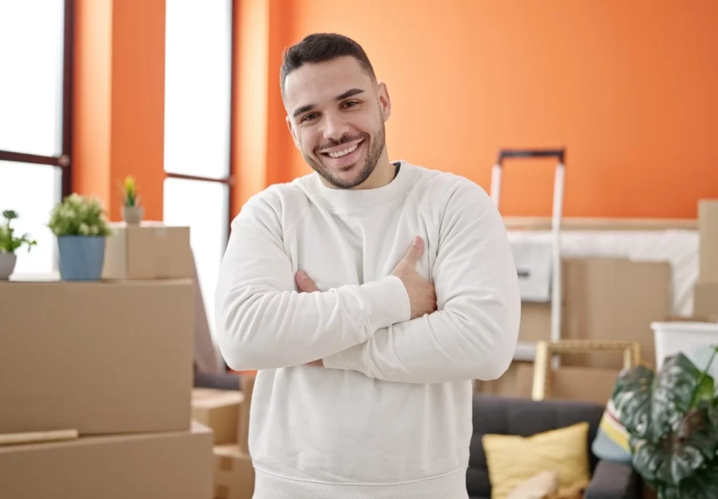 Happy man smiling at camera with arms crossed in front of moving boxes