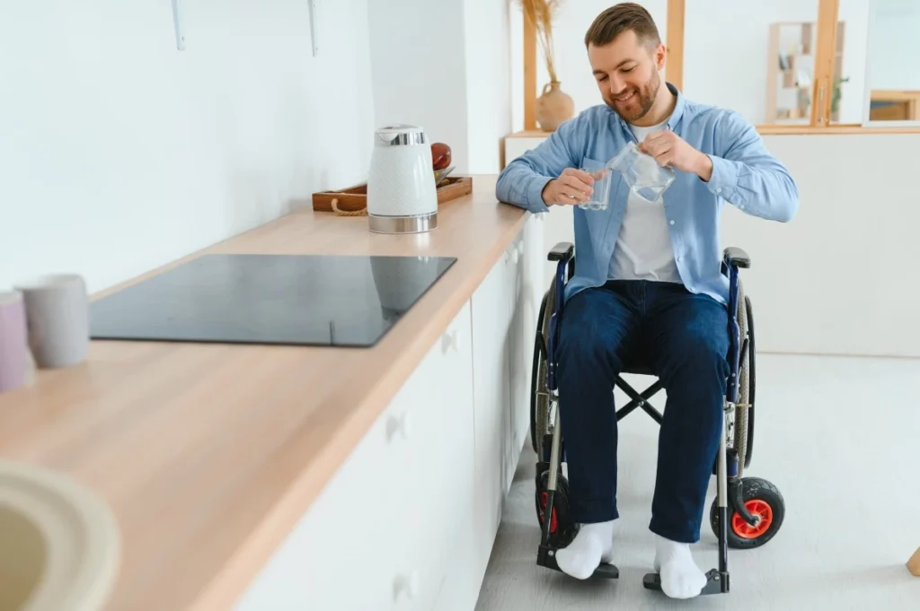 Disabled man in wheelchair in kitchen pouring himself a glass of water
