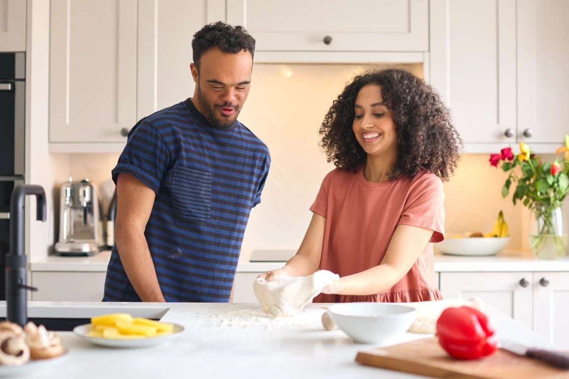 Man with Down syndrome making pizza dough with a support worker in a home kitchen
