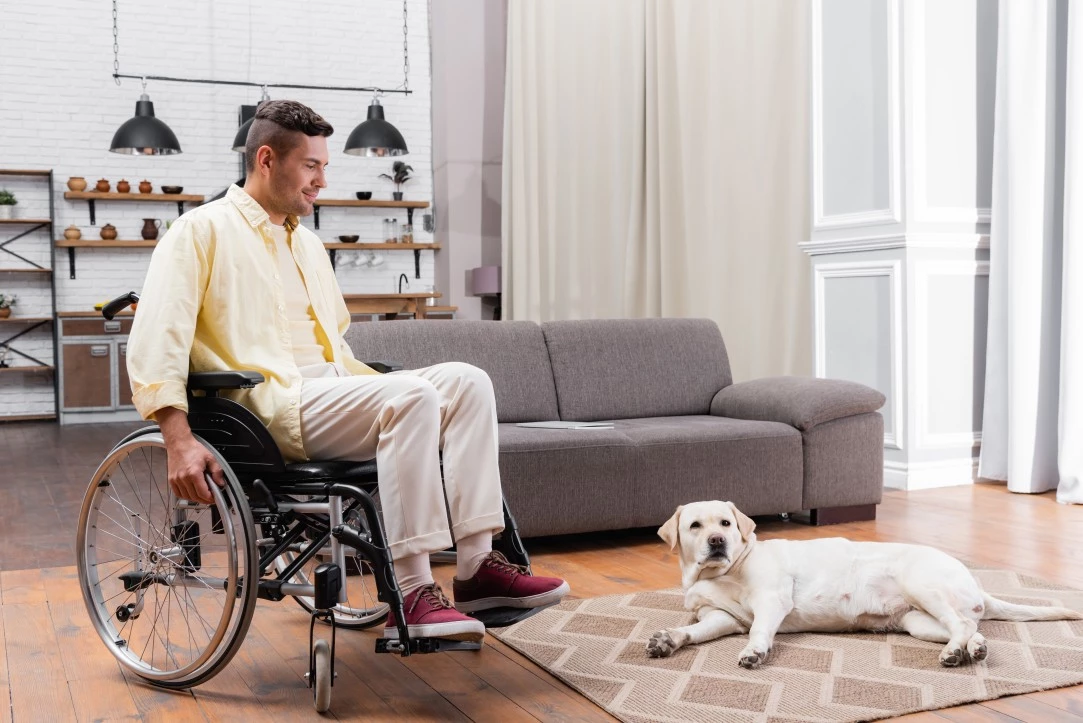 Man in a wheelchair sitting in a living room with a dog beside him