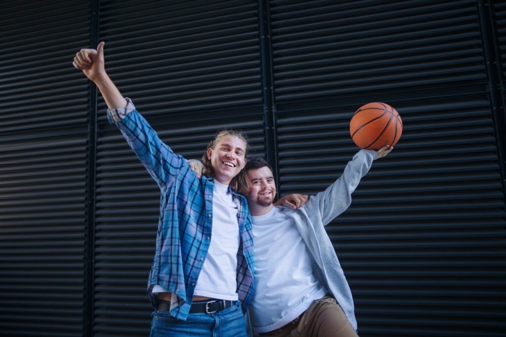 Disabled man with down syndrome holding basketball with support worker both smiling at camera
