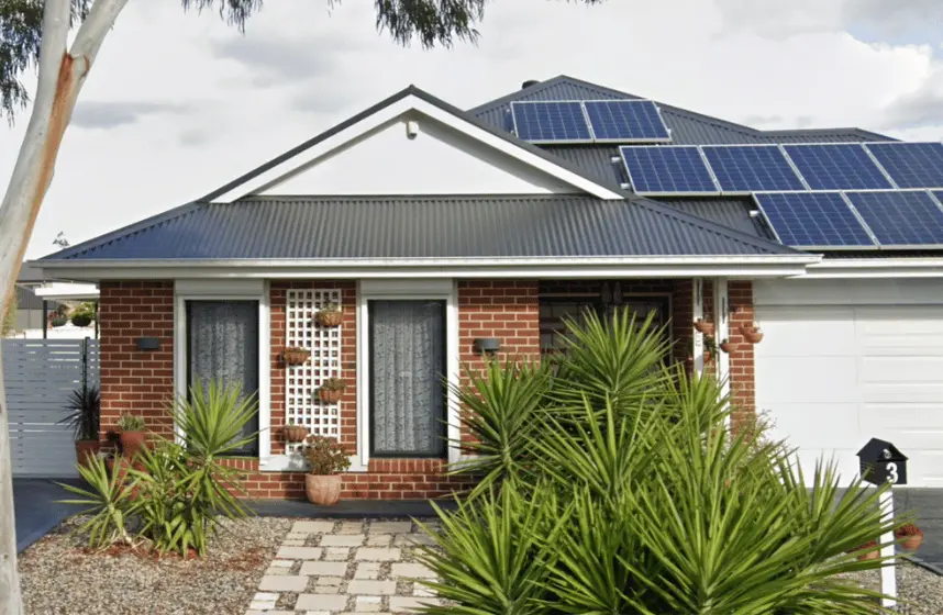 Image of front of red brick house with solar panels on roof and green plants out the front