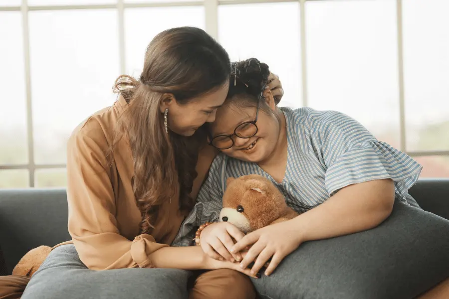 Happy disabled girl with down syndrome sitting on couch having a hug with family member