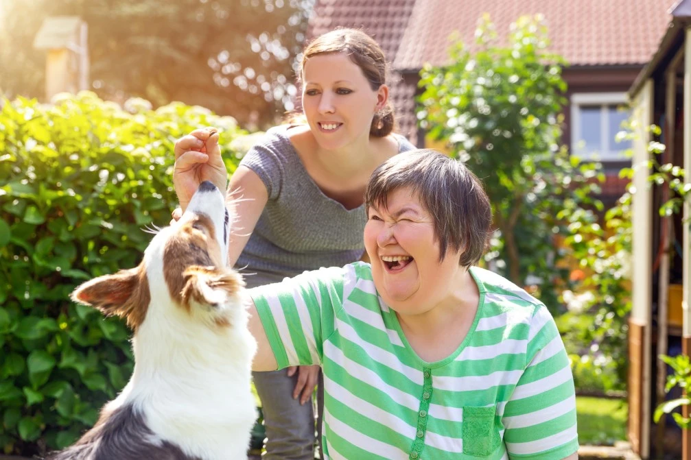 Disabled woman with support worker outside in yard giving dog treats