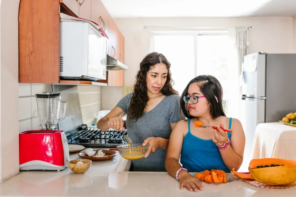 Disabled girl cooking in kitchen with support worker